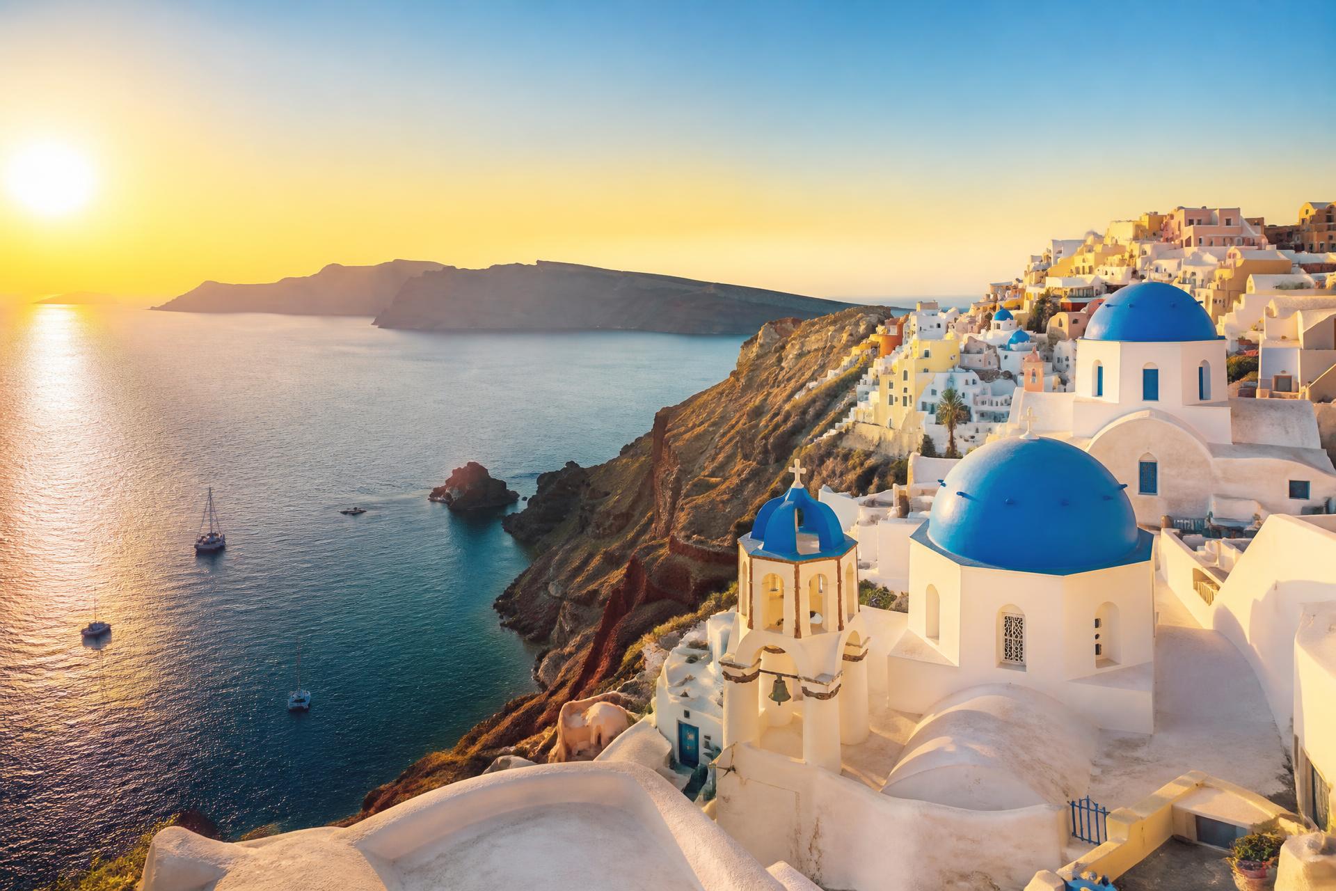 A Greek island at golden hour with blue-domed churches above the Aegean sea